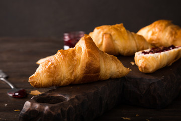 Delicious fresh mini croissants with fruit jam on wooden cutting board on old dark background. Healthy Breakfast with copy space.