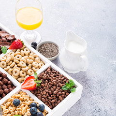 Fototapeta na wymiar Variety of cold quick breakfast cereals with berries in white wooden box, healthy eating for kids, selective focus.