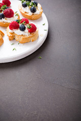 Sandwiches with fresh berries, goat cheese and honey on marble cutting board, copy space.