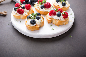 Sandwiches with fresh berries, goat cheese and honey on marble cutting board, copy space.