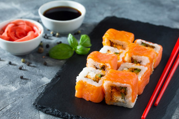 Roll Jamaica on a black slate board - tobiko orange salmon, salmon, soft cheese, cucumber, nori, rice.