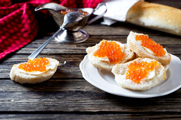 Snack, sandwiches with butter, red caviar, crispy baguette and white wine on a wooden background 