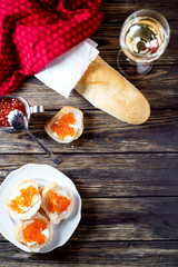 Fototapeta na wymiar Snack, sandwiches with butter, red caviar, crispy baguette and white wine on a wooden background 