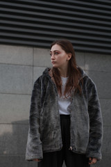 A beautiful and fashionable girl in a fur coat walks in the city on a sunny day