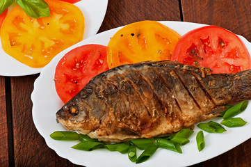 Roasted river fish carp on a white plate with tomatoes