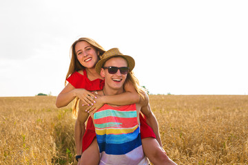 Happy Couple Having Fun Outdoors on wheat field. Laughing Joyful Family together. Freedom Concept. Piggyback