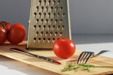 tomato on a cutting board next to a grater, fork and knife