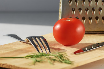 tomato on a cutting board next to a grater, fork and knife