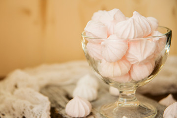 Gentle dessert. Meringues with taste of cranberries in a glass vase on a white tray on a light wooden table.