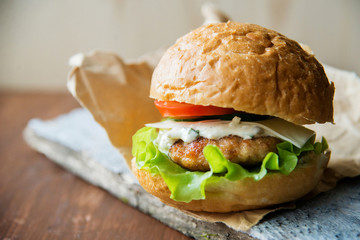 Close-up photo of home made hamburger with beef, onion, tomato, lettuce, cheese and spices. Fresh burger closeup on wooden rustic table with potato fries and chips.