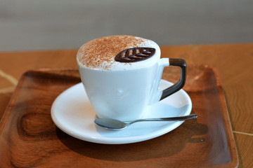 Delicious foamy cappuccino on a white cup on a plate.