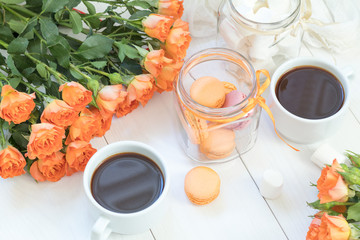 Orange mango macaroons, cup of coffee, marshmallow and fresh little roses on light wooden background. Sunlight. Coloring and processing photo with light vintage style. Shallow depth of field.