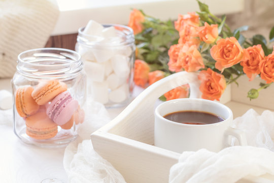 Orange mango macaroons, cup of coffee, marshmallow and fresh little roses on light wooden background. Sunlight. Coloring and processing photo with light vintage style. Shallow depth of field.