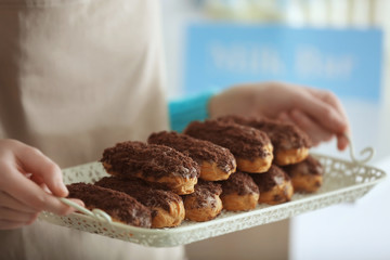 Woman hands holding delicious eclairs on metal tray