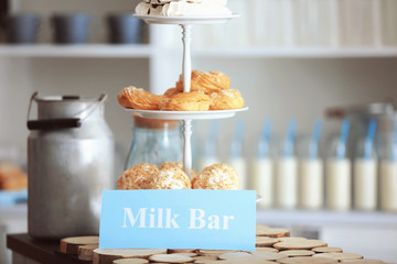Tasty desserts and card with text MILK BAR on table
