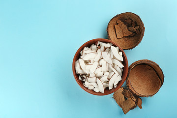 Bowl with coconut shavings and shell on color background