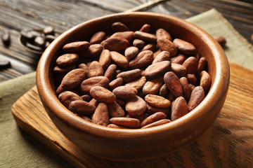 Bowl with aromatic cocoa beans on wooden background