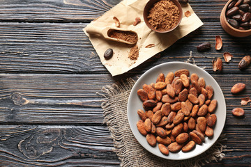 Plate with aromatic cocoa beans on wooden table