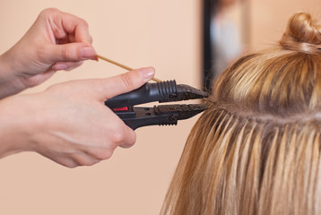 The hairdresser does hair extensions to a young girl, a blonde in a beauty salon. Professional hair care.