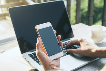 Girl holding smartphone and using laptop