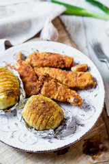 Hearty and delicious dinner, a baked potato with chicken sticks in crumbs, sauce, garlic and spices on a light wooden background 