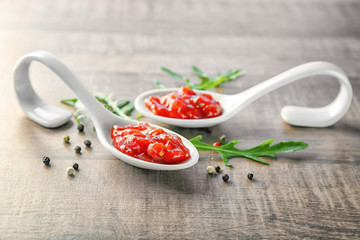Spoons with tasty chili sauce on wooden table