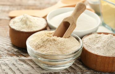 Bowls with different types of flour on wooden table, closeup