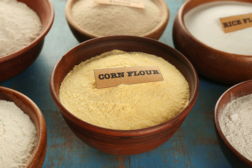 Bowls with different types of flour on grunge wooden background, closeup