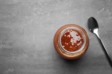 Jar with tasty caramel sauce and spoon on grey background