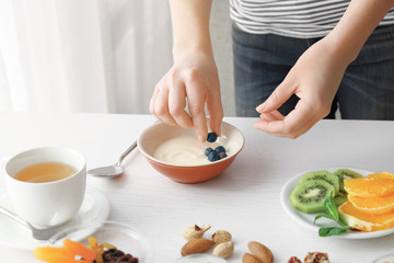 Woman putting berries into bowl with tasty yogurt on kitchen table
