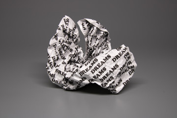 A crumpled paper with the words "dreams" written all over it on a grey background.