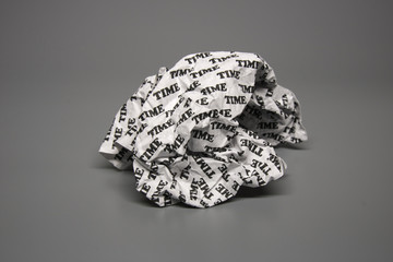 A crumpled paper with the word "time" written all over it on a grey background.