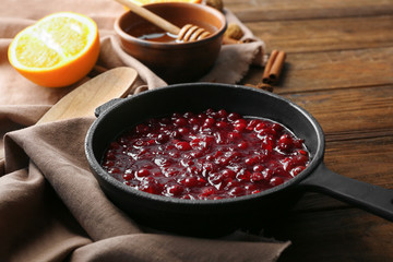 Delicious cranberry sauce in pan on wooden background