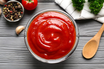 Delicious ketchup in bowl with ingredients on wooden background, top view