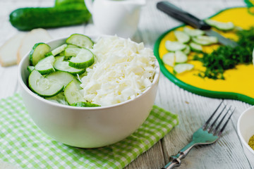  vegetarian Healthy food, light, low calorie fitness salad of fresh cucumbers, cabbage and dill with olive or sunflower oil, spices and salt on a light wooden background 