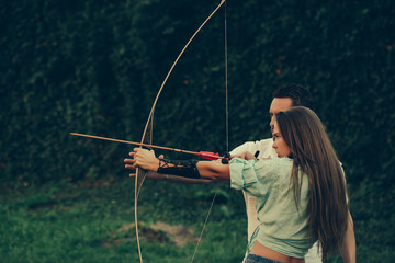 Cute girl and handsome man shooting with bow and arrow