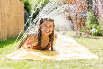 Water fun in garden - girl cooling down with water sprinkler
