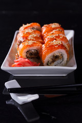 Japanese sushi rolls dish with chopsticks on black background