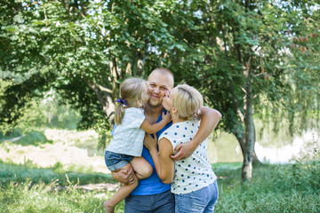 Naklejka na ściany i meble Happy joyful young family father, mother and little daughter having fun outdoors, playing together in summer park. Mom, Dad and kid laughing and hugging, enjoying nature outside. Sunny day, good mood