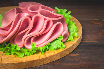 Sliced sausage with salad on a round wooden board.
