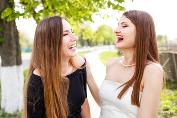 Two laughing ladies in cocktail dress standing outdoors. Young confident women with long hair have fun at the street