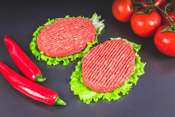 Raw burgers with lettuce on a gray background. Tomatoes, peppers