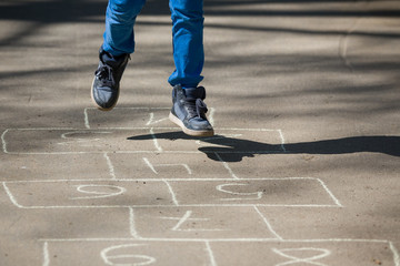 Fototapeta na wymiar Closeup of boy's legs and hopscotch drawn on asphalt. Child playing hopscotch on playground outdoors on a sunny day. outdoor activities for children.