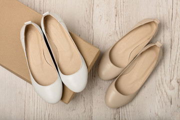 Women shoes (ballet flats) white and beige on a light wooden background.