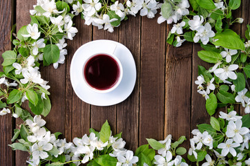Mug of tea among apple flowers on a wooden background. Top view