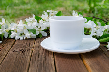 White mug on a wooden table, apple blossom on a background. Side view