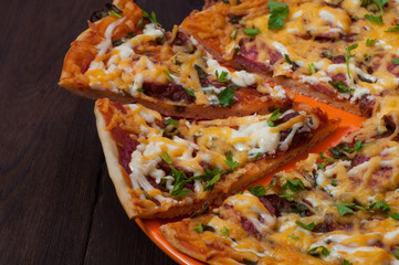 Pizza and two cut pieces on a dark wood background