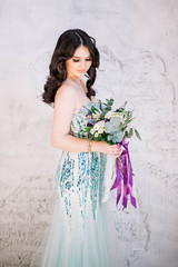 Beautiful girl bride brunette with professional makeup curls in a green lime dress with glitter sparkles with a delicate bouquet in his hand looking down with a smile on white background Studio