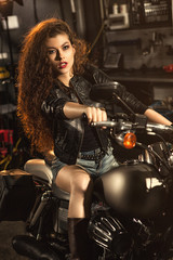 Naklejka na ściany i meble Beautiful young biker woman on her motorcycle at the workshop