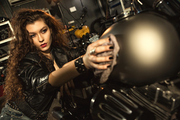 Fototapeta na wymiar Gorgeous young woman polishing her motorbike at the workshop